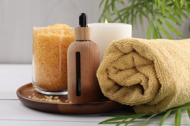 Photo of Spa composition. Bottle of cosmetic product, sea salt, burning candle and towel on white table, closeup