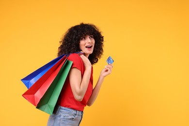 Photo of Happy young woman with shopping bags and credit card on yellow background
