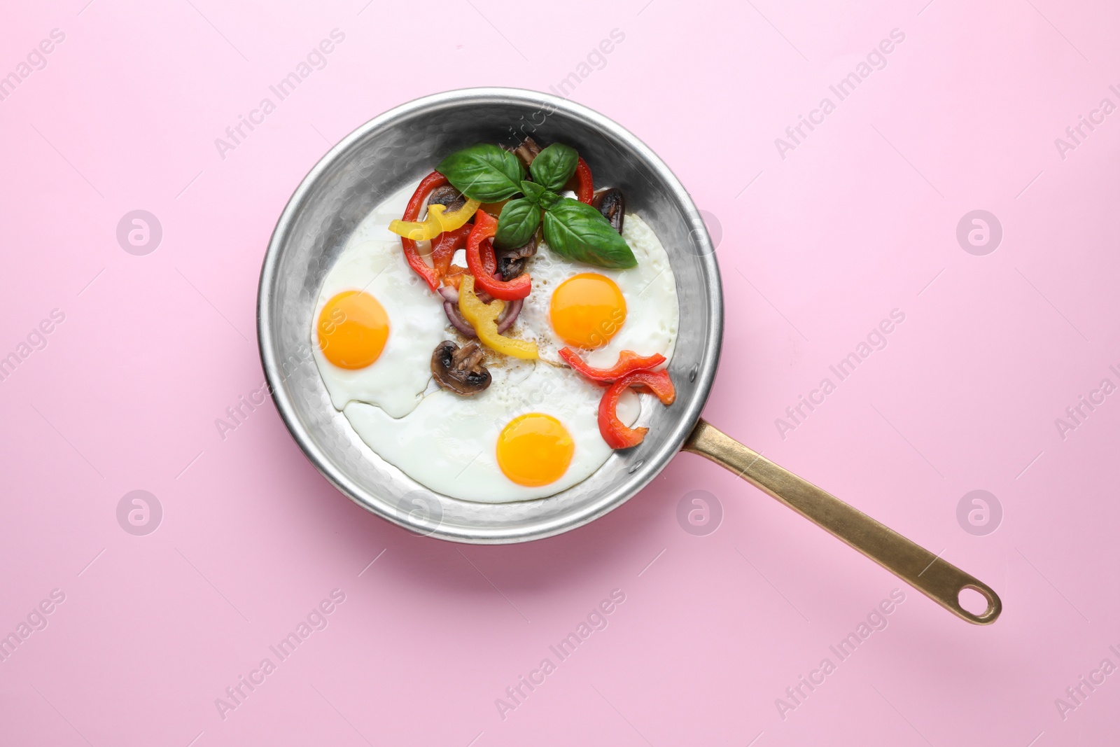 Photo of Tasty fried eggs with vegetables in pan on pink background, top view