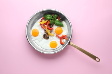 Photo of Tasty fried eggs with vegetables in pan on pink background, top view