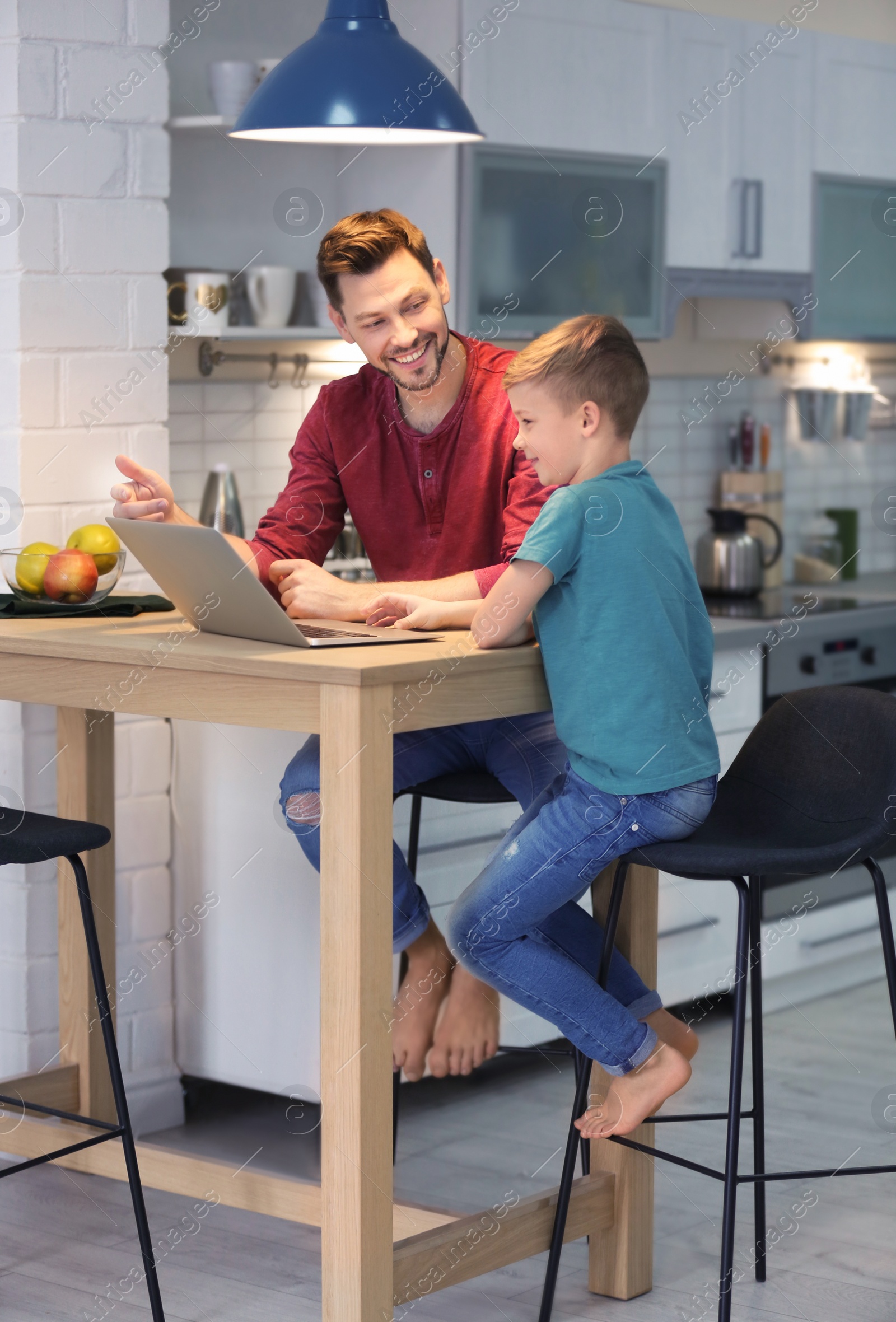 Photo of Little boy and his dad using laptop at home