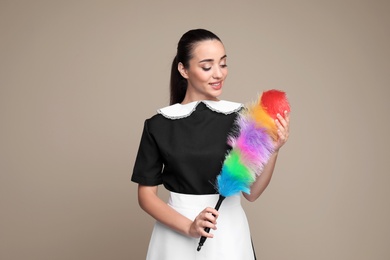 Photo of Young chambermaid with dusting brush on color background