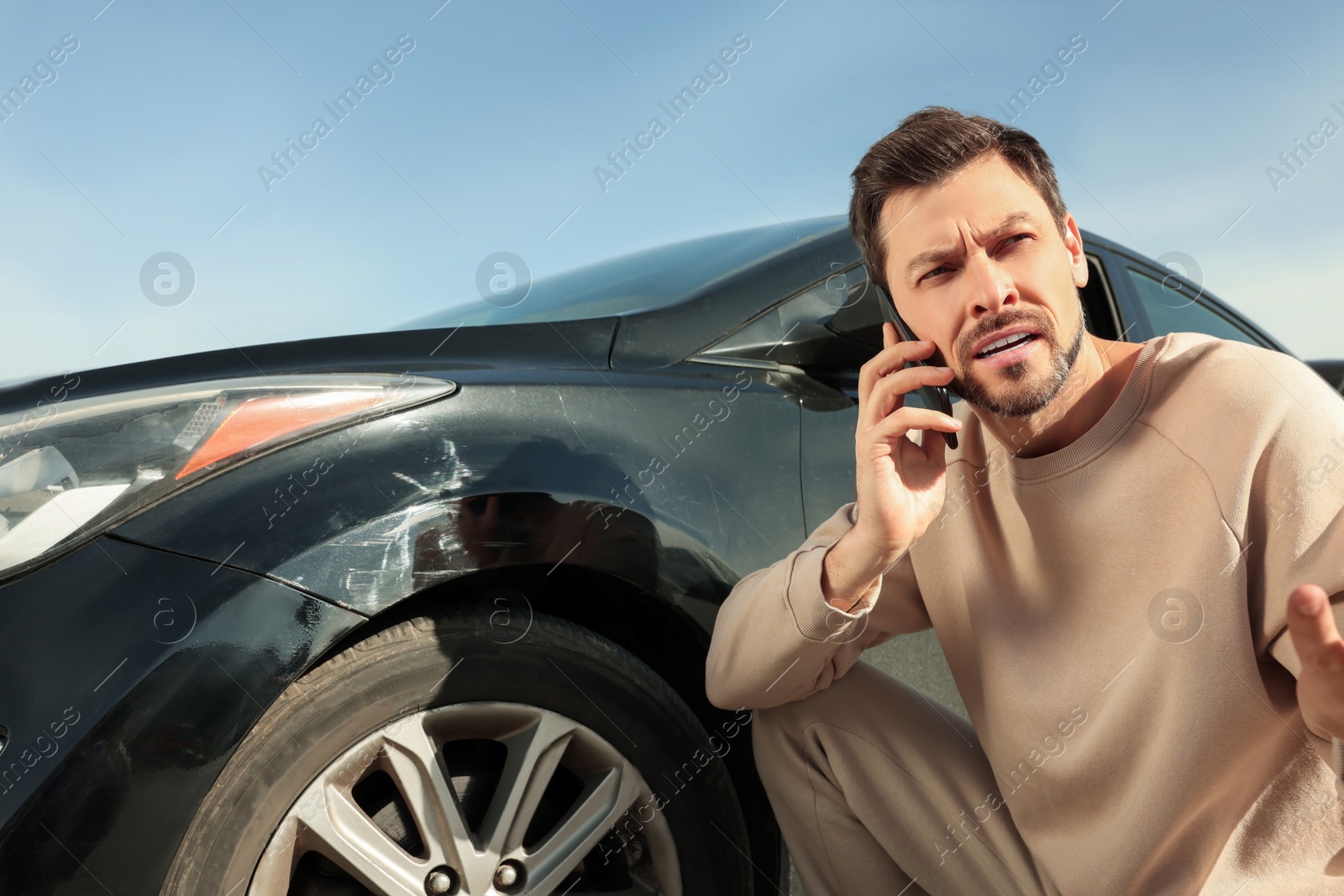 Photo of Man talking on phone near car with scratch outdoors