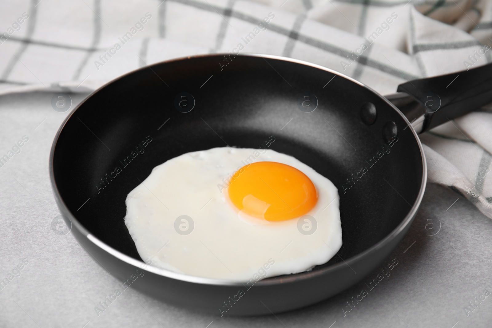 Photo of Tasty fried egg in pan on light grey table, closeup