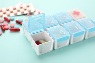 Photo of Plastic box with different pills on turquoise background, closeup