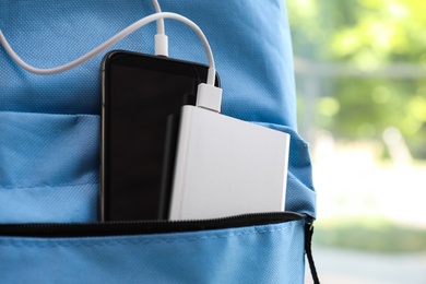 Photo of Charging mobile phone with power bank in light blue backpack, closeup