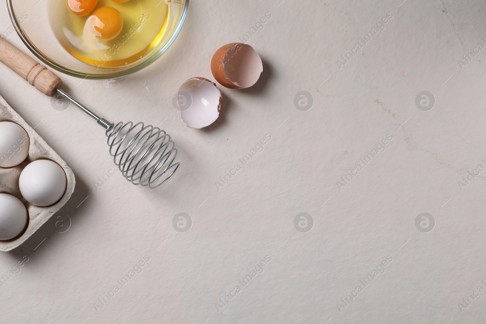 Photo of Metal whisk, raw eggs and shells on light table, flat lay. Space for text