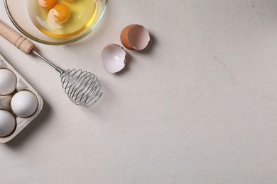 Metal whisk, raw eggs and shells on light table, flat lay. Space for text