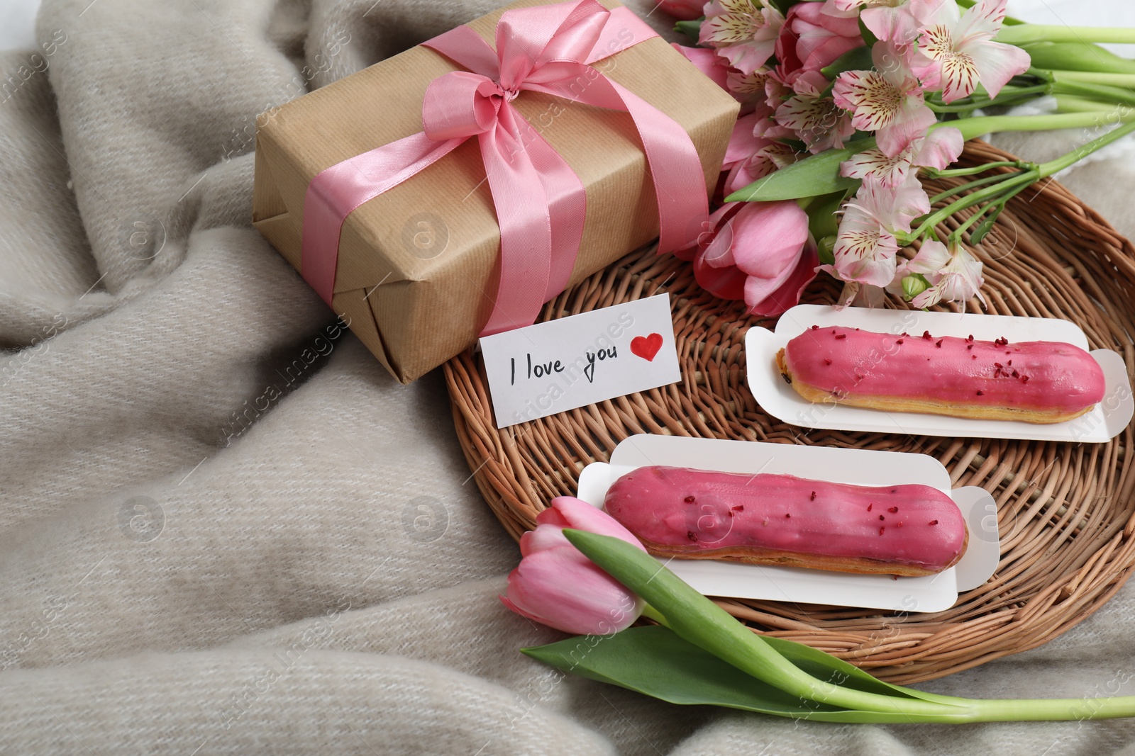 Photo of Tasty breakfast served in bed. Delicious eclairs, tea, flowers, gift box and card with phrase I Love You on blanket