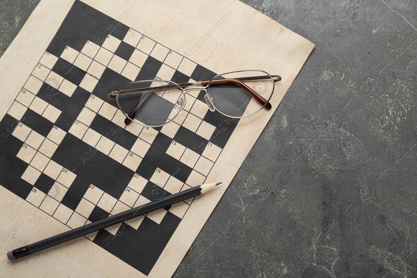 Photo of Blank crossword, glasses and pencil on grey table, top view. Space for text