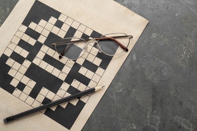 Blank crossword, glasses and pencil on grey table, top view. Space for text