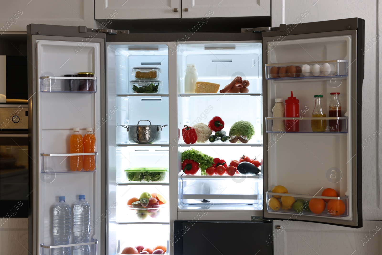 Photo of Open refrigerator full of different products in kitchen