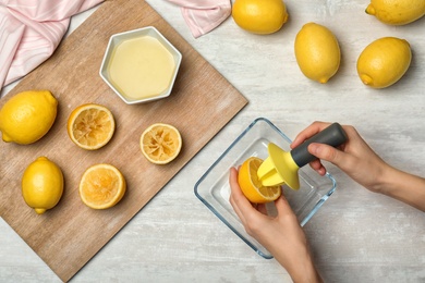 Woman squeezing fresh lemon juice with plastic reamer into bowl on table, top view