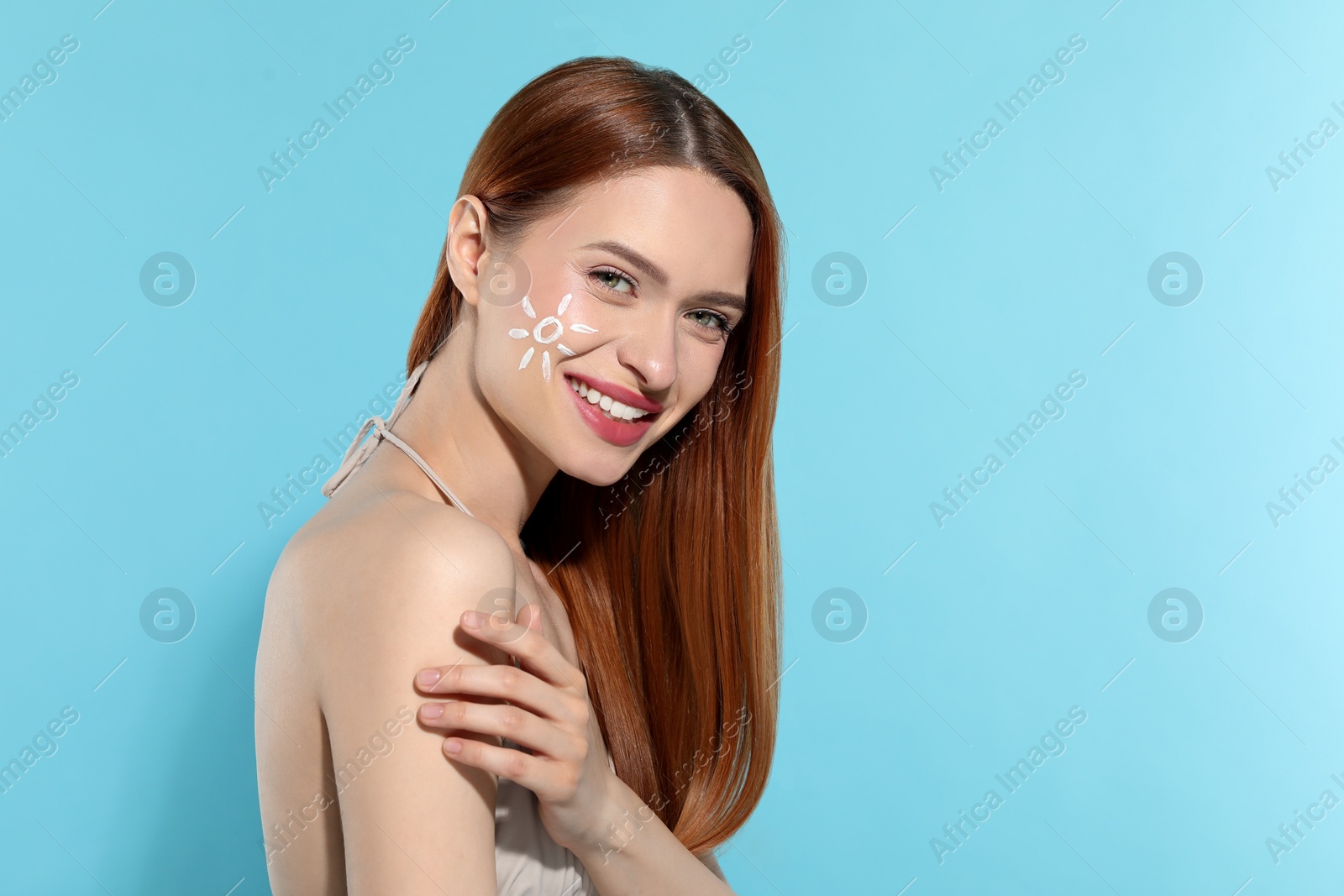 Photo of Beautiful young woman with sun protection cream on her face against light blue background, space for text