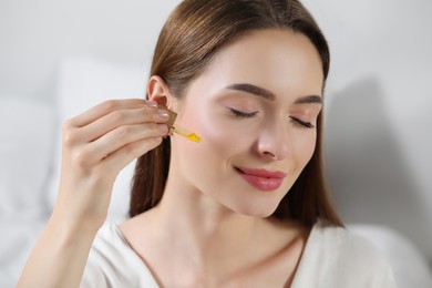 Photo of Young woman applying essential oil onto face on blurred background