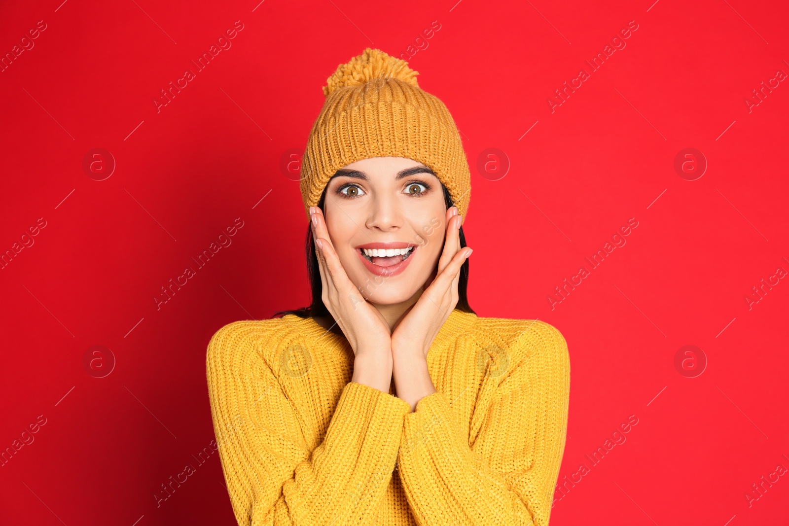 Photo of Excited woman wearing warm sweater and hat on red background. Winter season