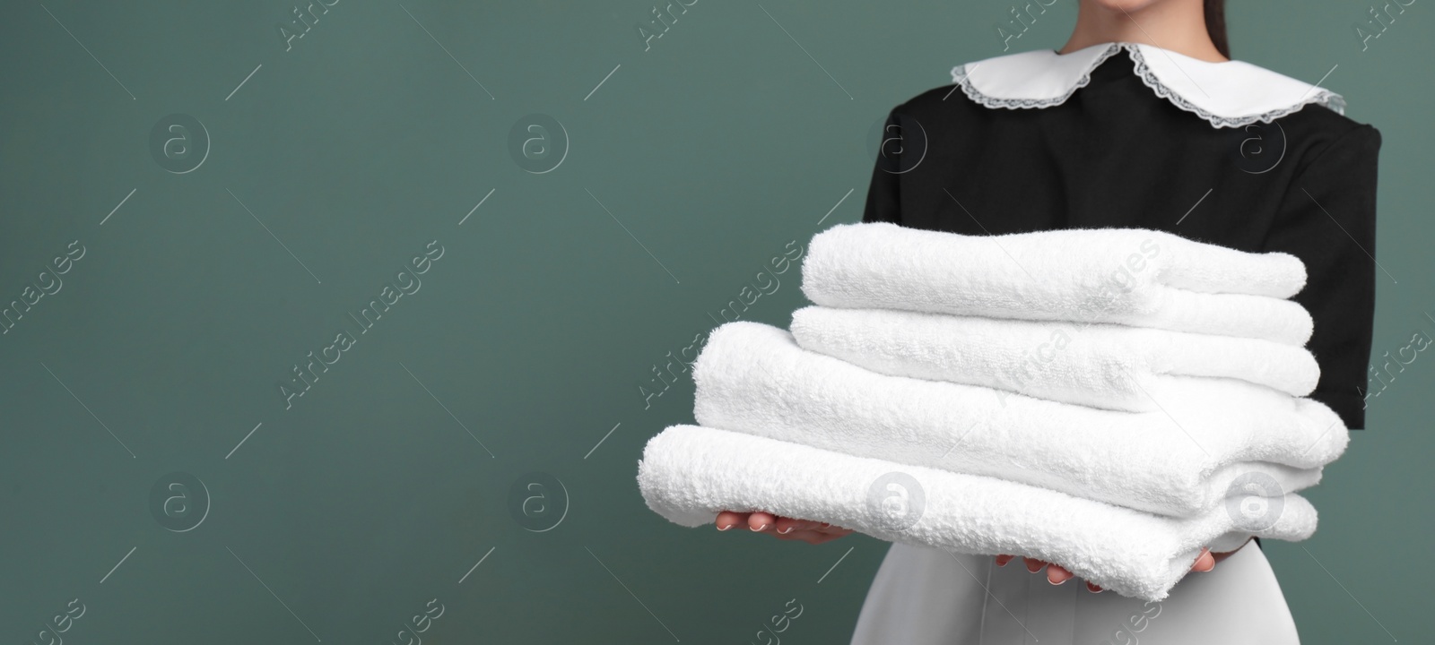 Image of Young chambermaid holding stack of clean towels on color background, closeup view with space for text. Banner design