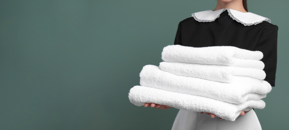 Image of Young chambermaid holding stack of clean towels on color background, closeup view with space for text. Banner design