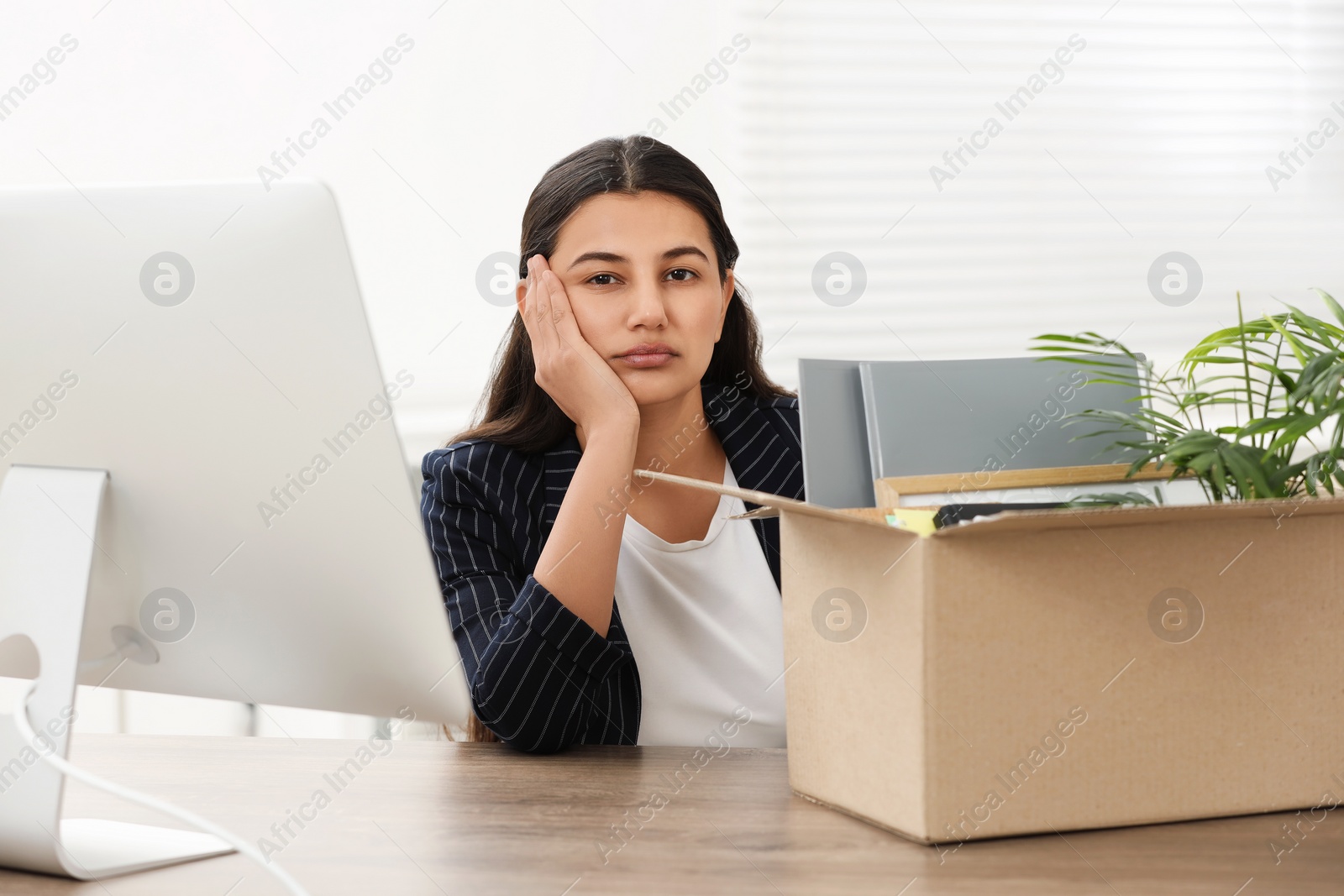 Photo of Unemployment problem. Woman with box of personal belongings at table in office