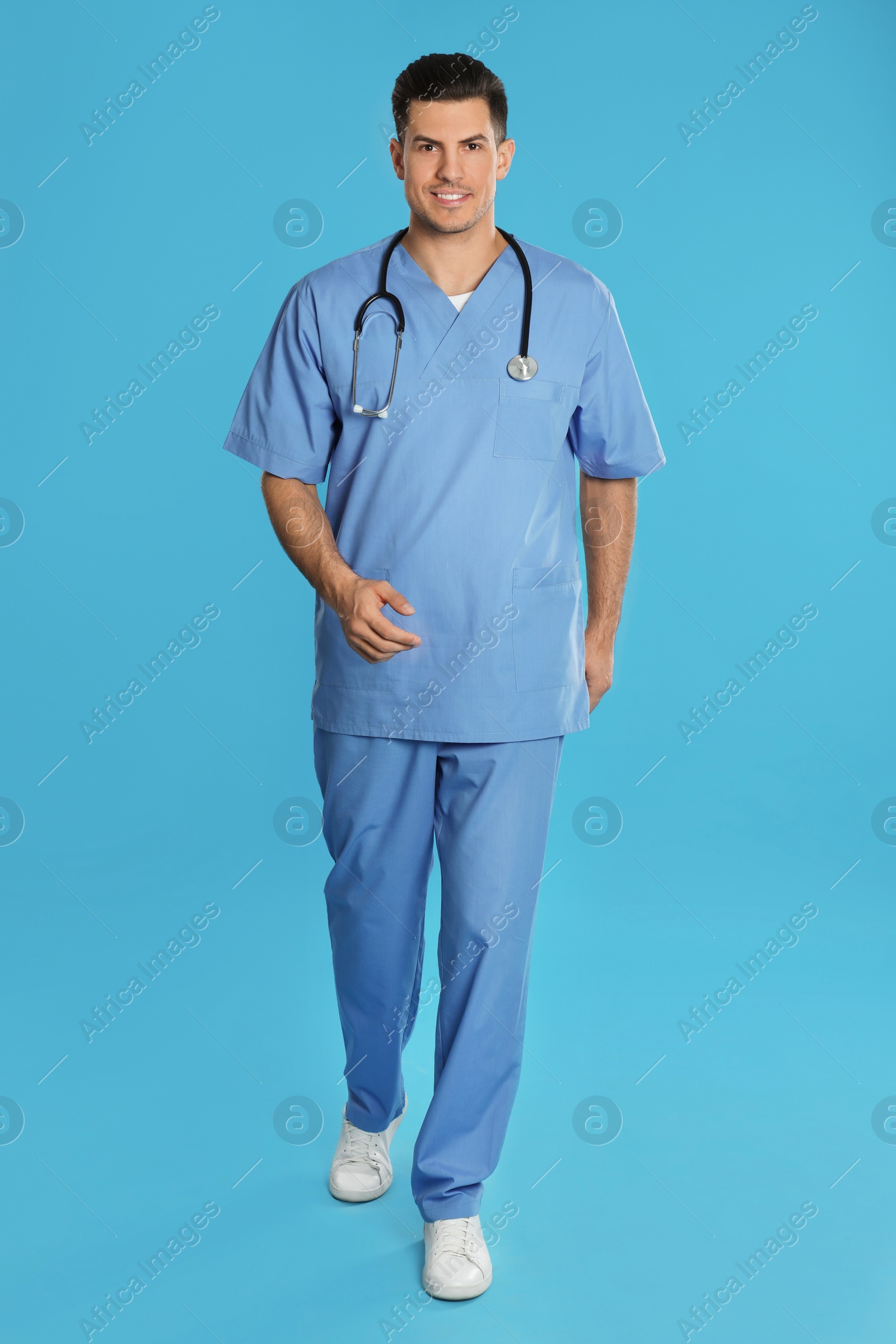 Photo of Handsome doctor in uniform walking on blue background