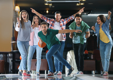 Photo of Young man throwing ball and spending time with friends in bowling club