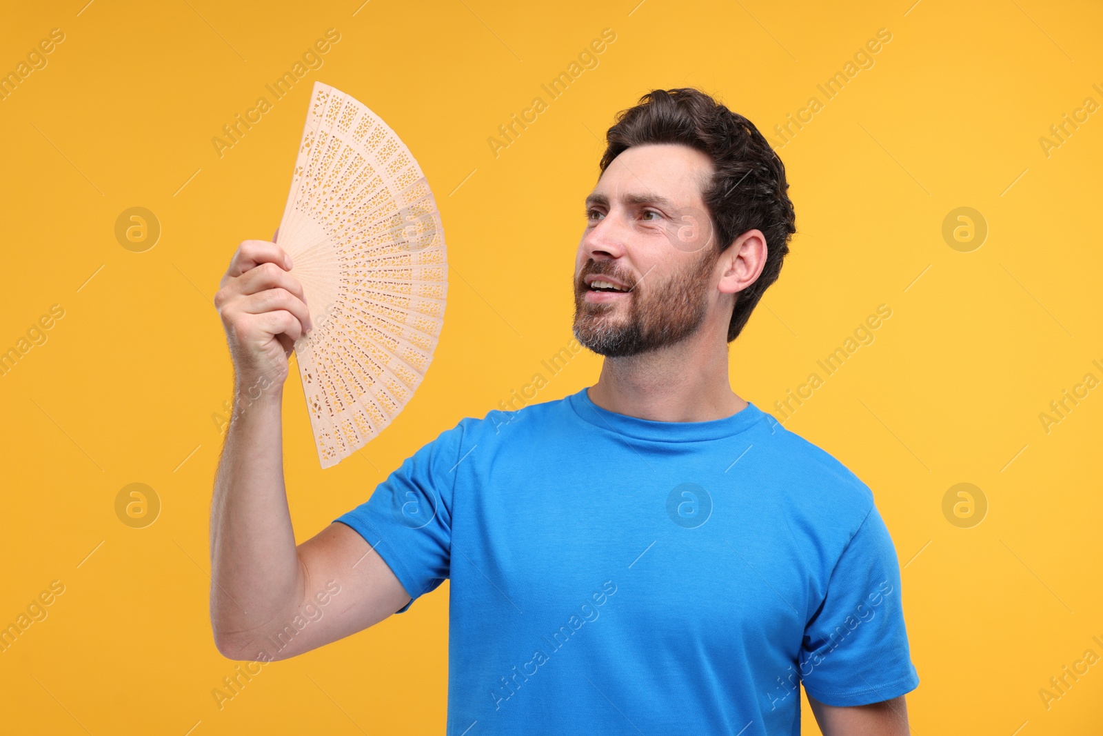 Photo of Happy man holding hand fan on orange background