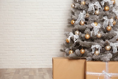 Photo of Decorated Christmas tree and gift boxes near white brick wall, closeup. Space for text