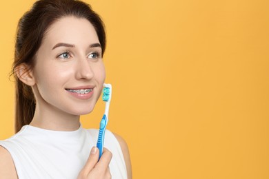 Photo of Portrait of smiling woman with dental braces and toothbrush on yellow background. Space for text