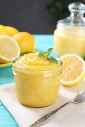 Delicious lemon curd in glass jar, fresh citrus fruits, mint and spoon on light blue wooden table