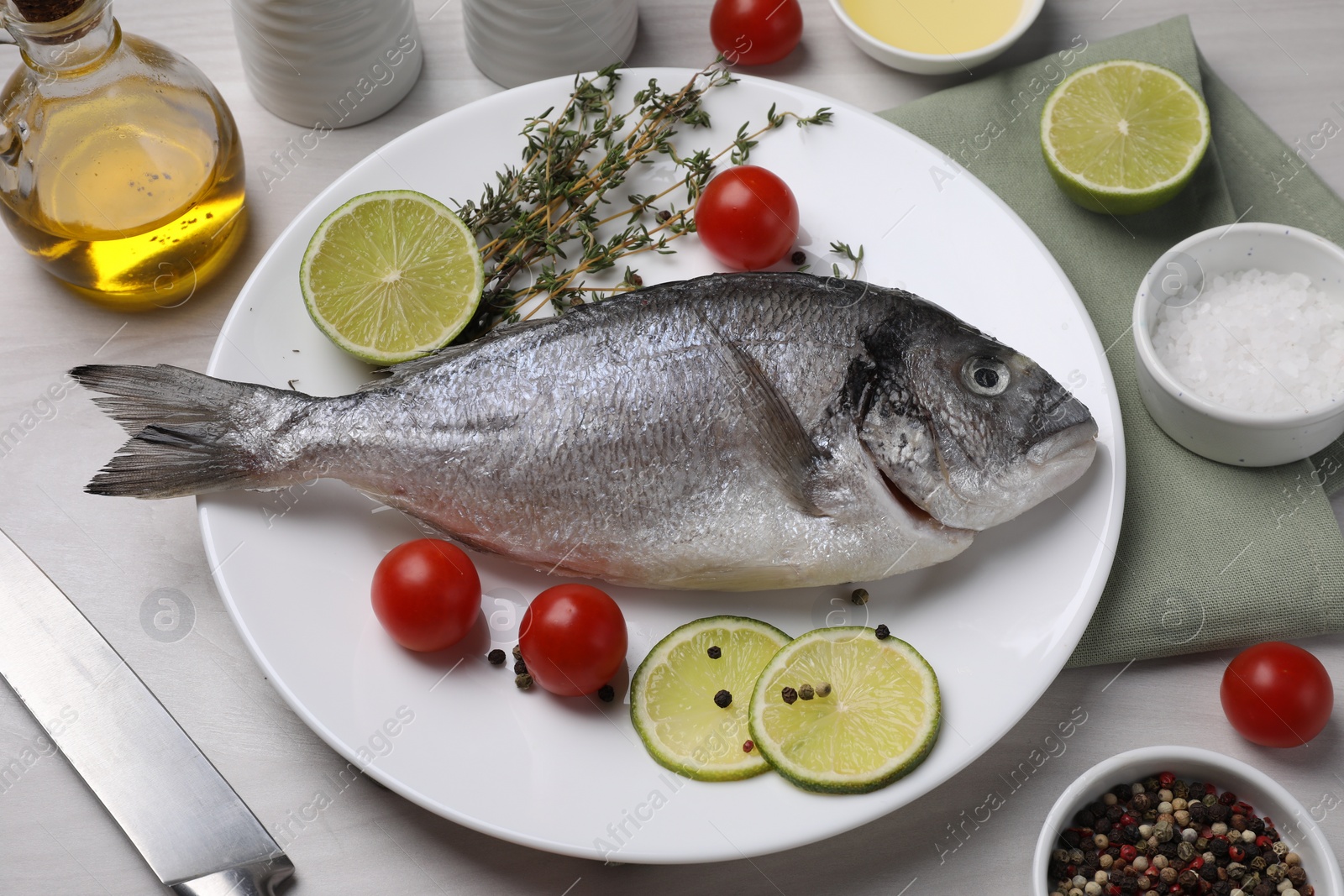 Photo of Raw dorado fish, lime slices, tomatoes and thyme on white table