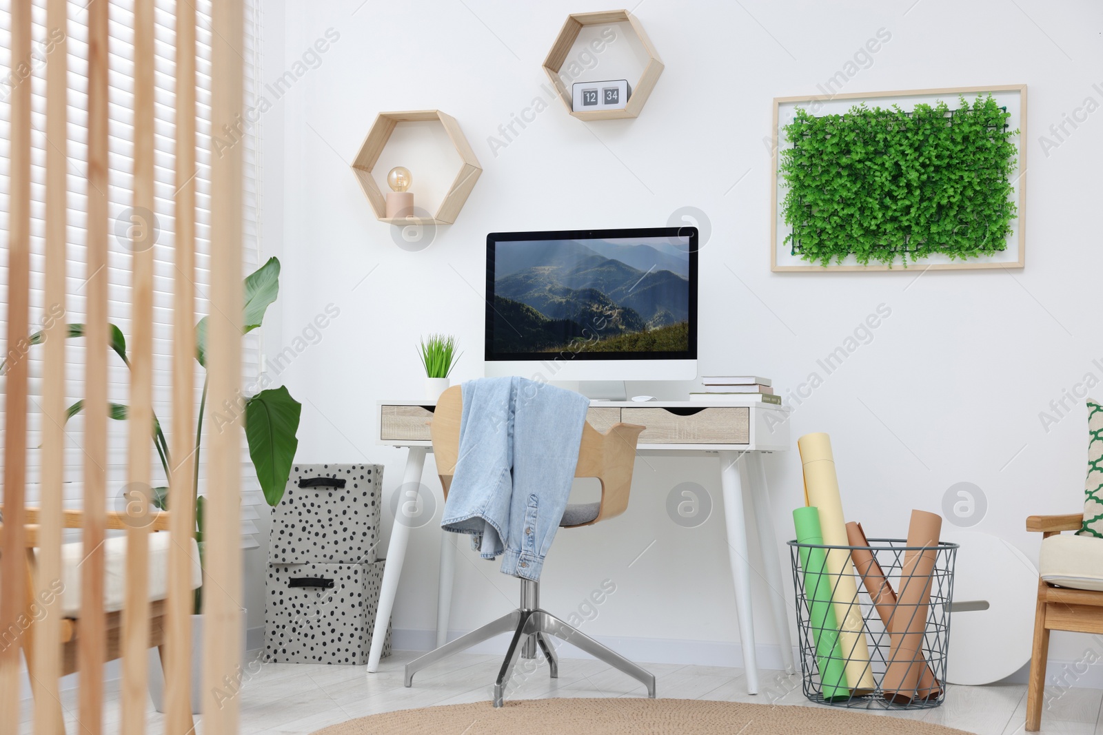 Photo of Green artificial plant wall panel and desk with computer in light room. Interior design