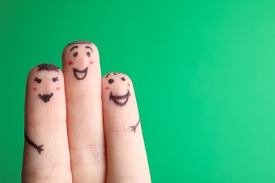 Photo of Three fingers with drawings of happy faces on green background, space for text