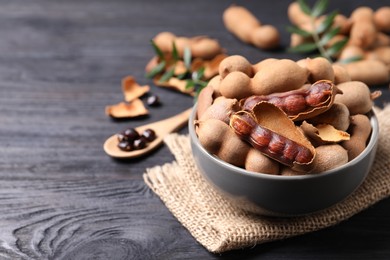 Photo of Delicious ripe tamarinds in ceramic bowl on black wooden table. Space for text