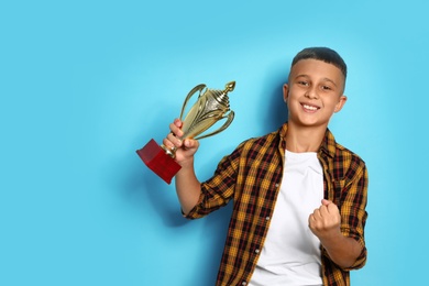Photo of Happy boy with golden winning cup on blue background