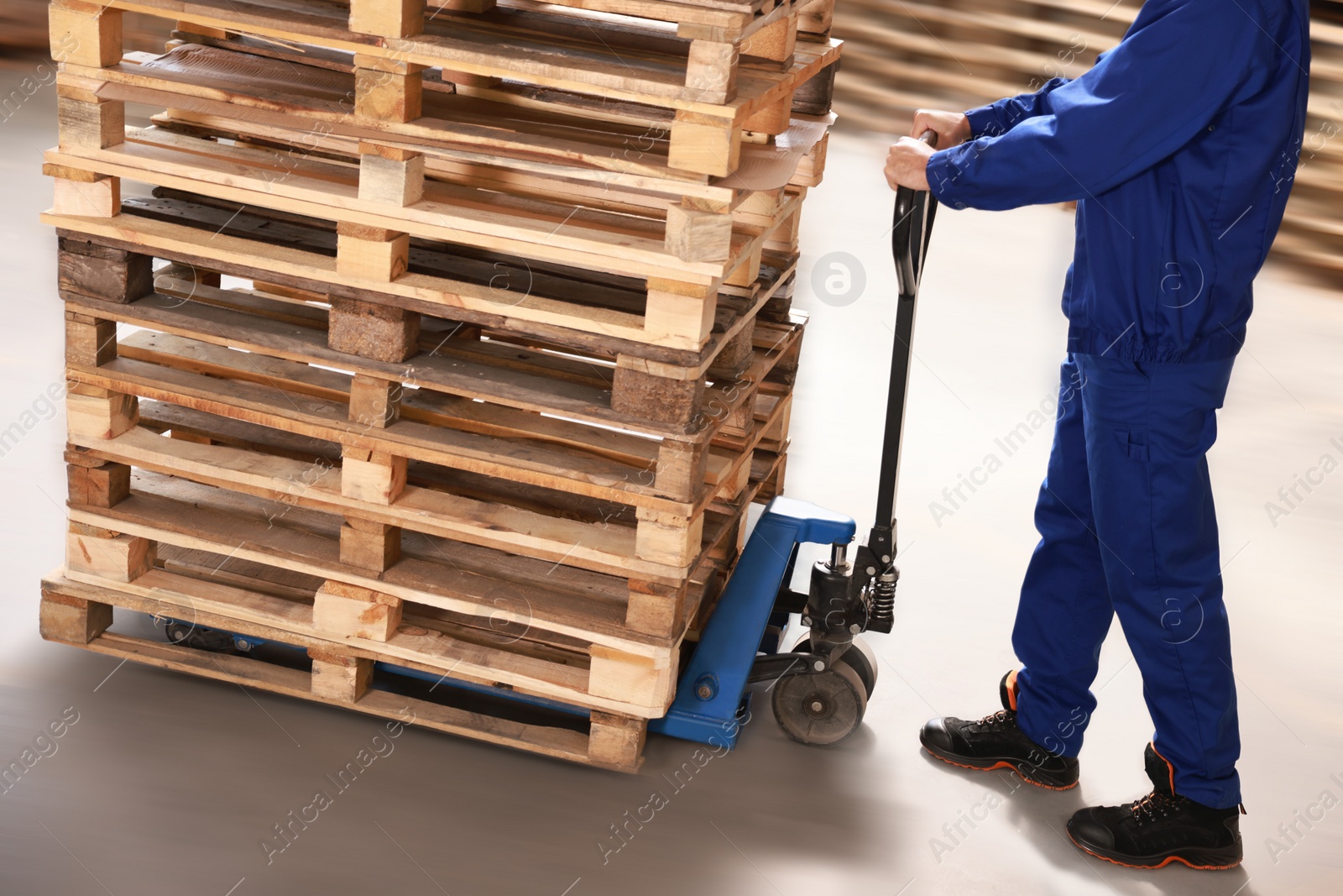 Image of Worker moving wooden pallets with manual forklift in warehouse, closeup