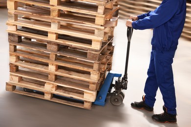 Image of Worker moving wooden pallets with manual forklift in warehouse, closeup