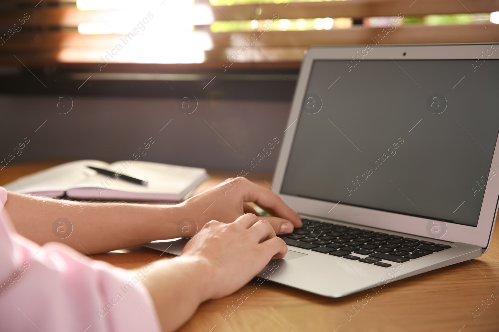 Photo of Woman using modern laptop at wooden table indoors, closeup