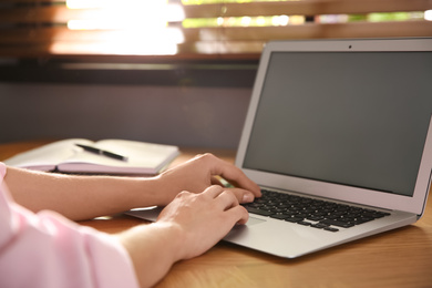 Photo of Woman using modern laptop at wooden table indoors, closeup