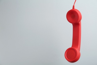 Red corded telephone handset hanging on light grey background, space for text. Hotline concept