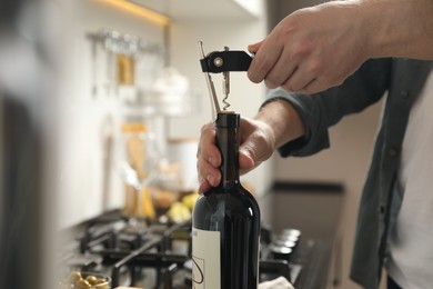 Man opening wine bottle with corkscrew indoors, closeup