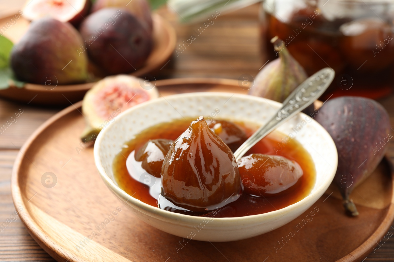 Photo of Bowl of tasty sweet fig jam on wooden table, closeup