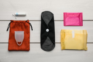 Photo of Cloth menstrual pad near other reusable and disposable female hygiene products on white wooden table, flat lay