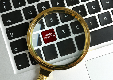 Image of Magnifying glass and computer keyboard with phrase CYBER BULLYING on black button, top view 