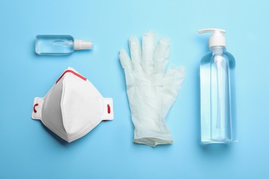 Medical gloves, respiratory mask and hand sanitizers on light blue background, flat lay