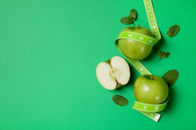 Fresh apples, mint leaves and measuring tape on green background, flat lay. Space for text