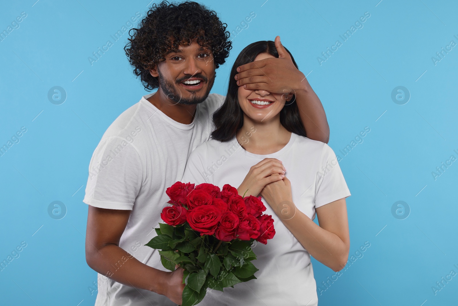 Photo of International dating. Handsome man presenting roses to his beloved woman on light blue background