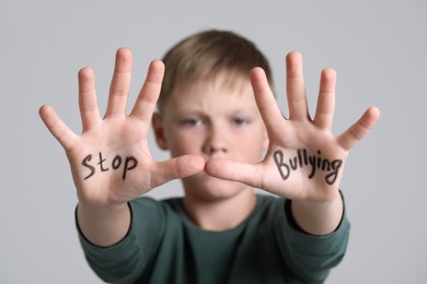 Boy showing hands with phrase Stop Bullying on light grey background, selective focus