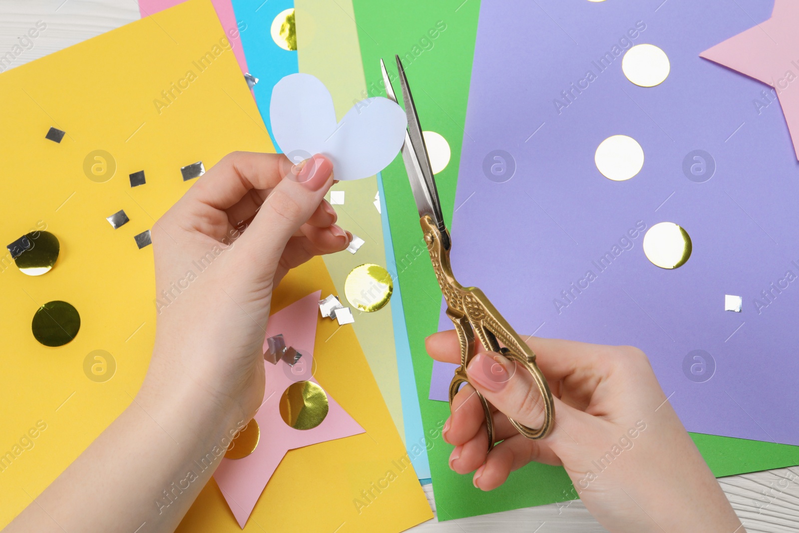 Photo of Woman cutting paper heart with scissors at white wooden table, top view