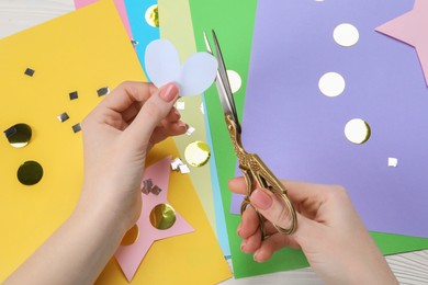 Woman cutting paper heart with scissors at white wooden table, top view