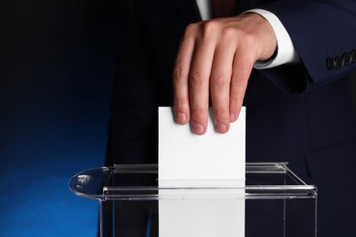 Man putting his vote into ballot box on dark blue background, closeup. Space for text